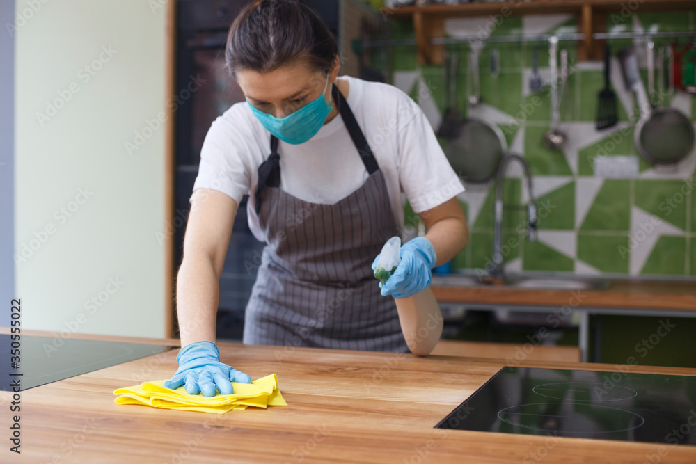 Woman in protective mask and gloves cleaning kitchen - obrazy, fototapety, plakaty 