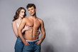 © LIGHTFIELD STUDIOS - woman touching muscular boyfriend standing with hands in pockets on grey