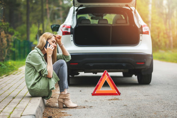 woman is sitting on the side of the road and calling for help because car accident