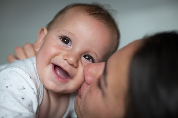 Wall Mural - Authentic  close up shot of an young happy neo mother is playing with her smiling newborn baby boy on a bed just woke up in a morning.  