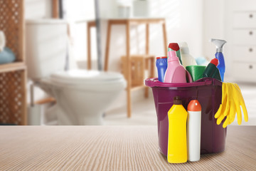 Poster - Bucket with cleaning supplies on wooden table in bathroom, space for text