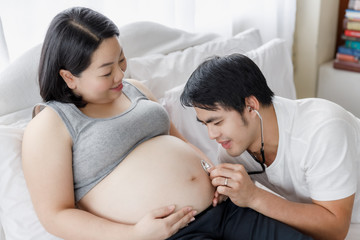 husband use a stethoscope to listen to sound of baby in belly of pregnant wife