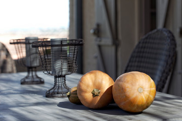 On the terrace of a property in the south of France, three pumpkins are arranged on the dining table dava,t two candleholders.