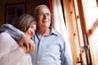 coppia di anziani si abbraccia felice e sorride in piedi nel salotto di casa
