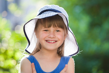 Wall Mural - Close-up portrait of happy smiling little girl in a big hat. Child having fun time outdoors in summer.