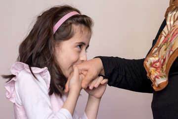 Little baby girl kiss her grandmother's hand during Eid mubarak (Turkish Ramazan or sacrifice feast). Adorable child kiss elderly woman hand to show respect. Cute girl follow muslim Ramadan traditions