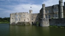 Flag Blows In Wind Atop Impressive Castle With Moat In Sunshine