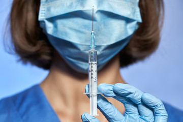 Syringe with medicine, vaccine for Coronavirus disease COVID-19 or another disease closeup, in hands of doctor in mask and surgical gloves