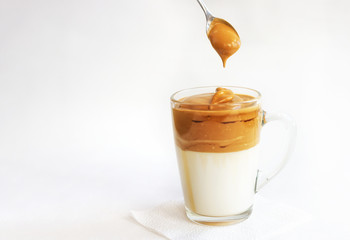 A trendy Korean drink. On a white background, a glass of whipped coffee and milk. Dalgona coffee. A whipped froth hangs from the spoon. Close-up, copyspace