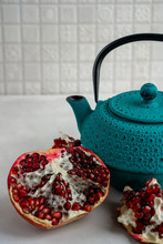 Half Of A Ripe Juicy Pomegranate And Blue Cast Iron Tea Pot Are Standing On A Cement Surface At Kitchen