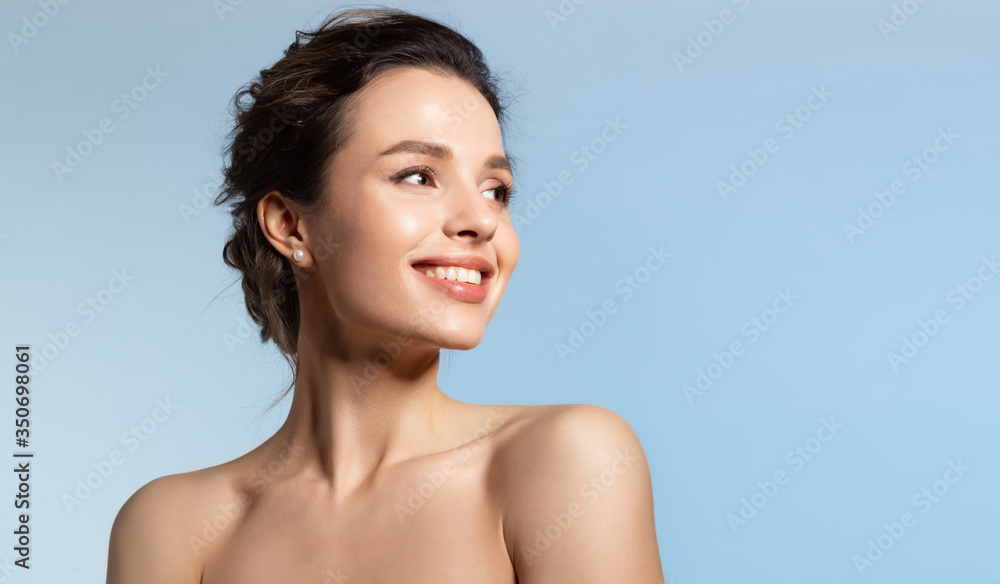 Toothy smiling young woman with shiny glowing perfect facial skin and bare shoulder looking aside. - obrazy, fototapety, plakaty 