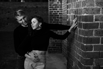 Romantic couple young beautiful sensual redhead woman and tall handsome blonde man posing in sunset sunlight on brick wall background in black and white