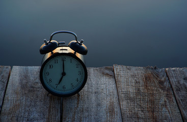 Summer time concept. Alarm clock on wooden bridge on sea sunrise background