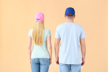 Wall Mural - Young couple in stylish caps on color background, back view