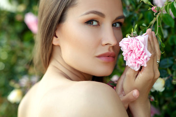 Beautiful young woman in nature in roses. Brunette girl with roses.