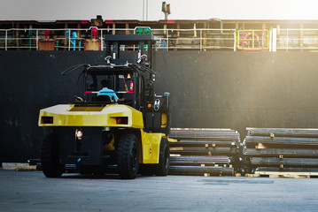 Wall Mural - Large forklift lift stack of steel bar beside vessel at a seaport. Cargo discharging from ship 