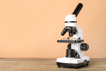 Modern microscope on table against color background