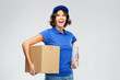 © Syda Productions - mail service and shipment concept - happy smiling delivery girl in blue uniform with parcel box and clipboard over grey background
