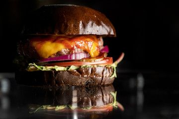 Wall Mural - Black Burger with Cheese, salad and onion with tomato ketchup. Cheeseburger with black bun on dark background.