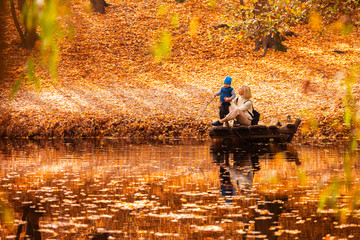 Happy young mother and her son spending time in the autumn park near the pond.