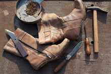 old torn boots and a shoemaker's tool on a wooden surface