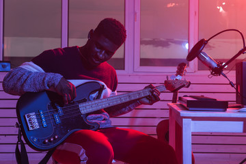 Wall Mural - Create music and a recording studio concept - African american man guitarist recording electric bass guitar track in home studio