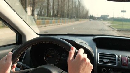 Canvas Print - Close up view of woman hands holding steering wheel driving a car on city street on sunny day.