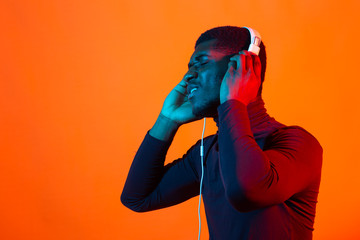 Wall Mural - Young african-american man's listening to music in headphones in neon light. Male portrait. Concept of human emotions, facial expression, holidays or weekend, hobby,