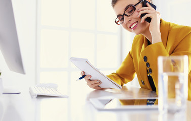 Portrait of beautiful woman making call while sitting at her workplace in front of laptop and working on new project