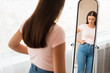 Unhappy Woman Gaining Weight Touching Belly Standing At Mirror Indoors