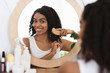 Smiling black woman combing her beautiful curly hair near mirror in bathroom
