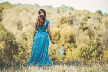 Sticker - beautiful romantic girl enjoying nature with fluffy feather grass in hands, young elegant woman looking into the distance, bride in blue long dress