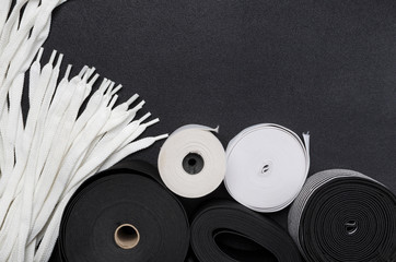 Top view of white and black sewing elastic, shoelaces on the wblack surface.E,pty space. Tools for making clothes