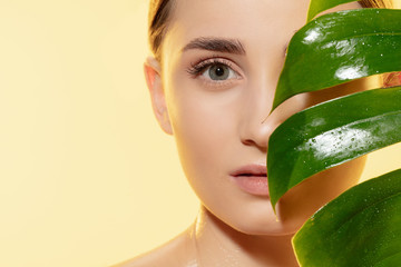 Wall Mural - Close up of beautiful young woman with green leaves on white background. Concept of cosmetics, makeup, natural and eco treatment, skin care. Shiny and healthy skin, fashion, healthcare.