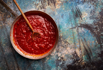 Wall Mural - Classic homemade Italian tomato sauce with basil for pasta and pizza in the pan on blue background, top view.