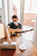 © LIGHTFIELD STUDIOS - high angle view of man in medical mask holding guitar and using laptop at home