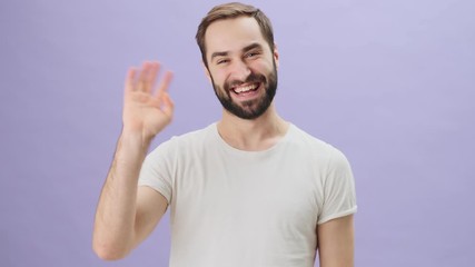 Poster - A friendly positive young man wearing a white t-shirt is waving his hand doing hello gesture with a smile standing isolated over gray background