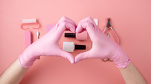 Women's Hands In Pink Gloves Hold Heart-shaped Hands Over Bottles Of Nail Polish And Manicure And Pedicure Tools. The Concept Of Love For Your Work And A Beautiful Manicure