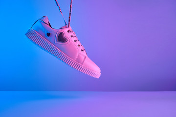 Wall Mural - Trendy white teenage sneakers with flying laces in trendy neon light. New shoe in retro surreal red, blue gradient light