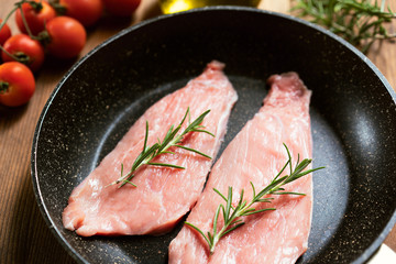 Raw  Veal Meat Steaks on a pan, tomatoes, rosemary, oil, garlic. Wooden background, side view 