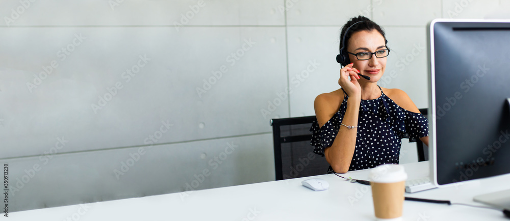 Beautiful consultant of call center in headphones.  Portrait of smiling female customer using headset at call center office - obrazy, fototapety, plakaty 