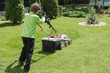 © Anna - boy mows grass in the yard with a lawn mower. the child helps adults in everyday activities. teaching children to work. home and garden activities concept