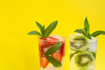Wall Mural - Infused water or lemonade with strawberry, kiwi, ice and  mint  in the two glasses  on the  yellow  background. Closeup. Copy space.