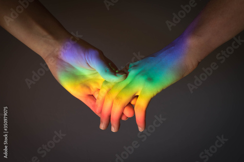 Two women holding hands, illuminated with the light of the LGBT rainbow flag. Gay pride concept. Lesbian love concept