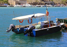 Two Blue, Small Motor Boats Are Standing At The Pier, The Engines Of The Boats Are Raised From The Water. Against The Background Of The Marina. Lifebuoys Are Attached To The Sides Of Boats For Safety.