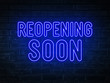 Reopening soon  - blue neon light word on brick wall background	
