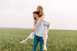 © Bostan Natalia - Young couple of man and woman playing in an open field, outdoors, on clean white background. Man gives a piggyback riding to woman, laughing.