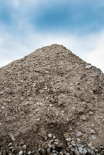A Large Pile Of Sandy Soil With A Stone. Above, You Can See Blue Sky And White Clouds. Construction.