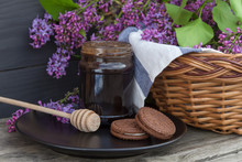 A Jar Of Honey Or Jam With Wicker Basket With Lilac On Wooden Background.