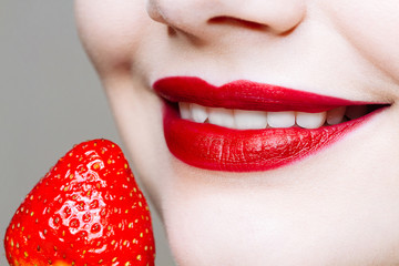 Macro close up of caucasus woman's lips with red lipstick and fresh strawberry.